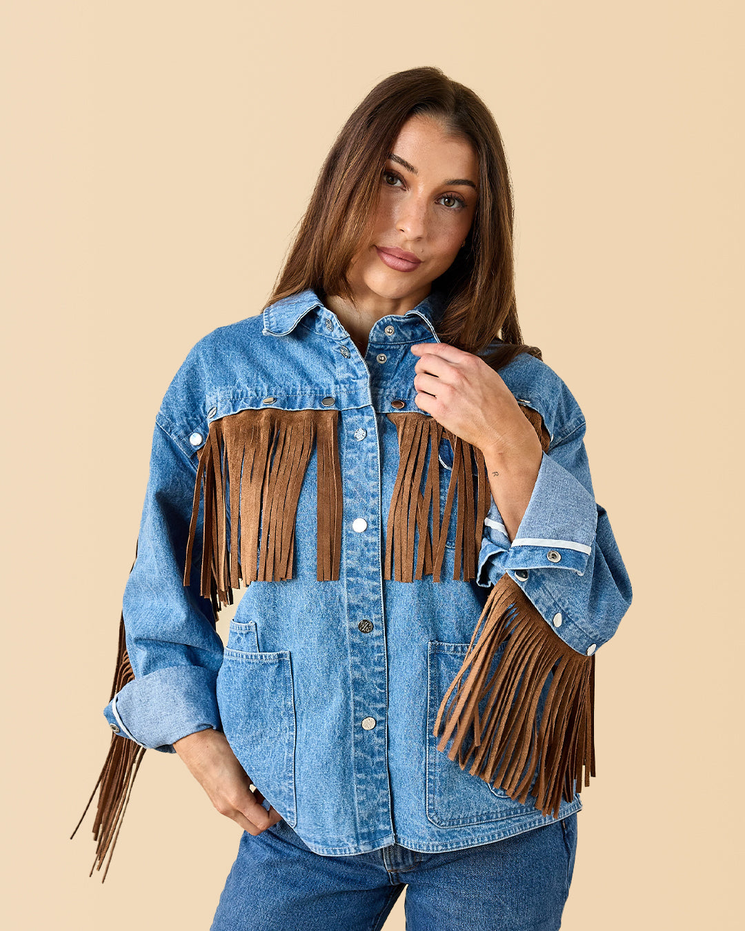 Woman wearing a blue denim jacket with brown fringes on a beige background