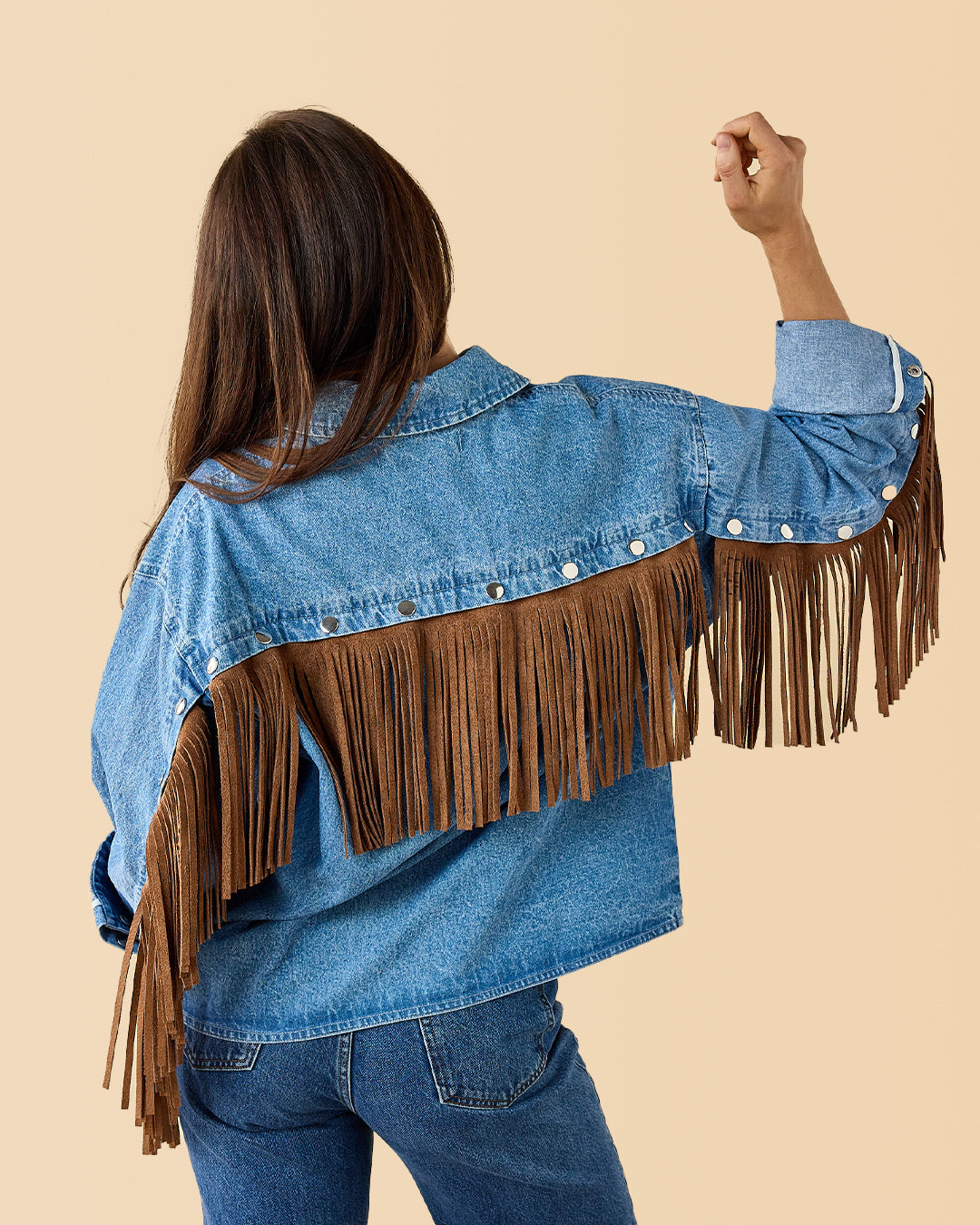 Person wearing a blue denim jacket with brown fringe on a beige background customizable fringe collegiate & high school colors